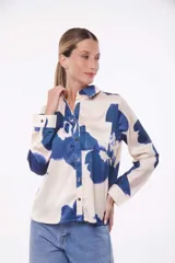 Camisa de manga larga color crema con estampado de flores azules, cuello clásico, cierre con botones y bolsillo en el pecho.