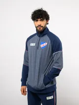 Buzo deportivo de medio cierre marca Umbro del Club Nacional de Football. Presenta un diseño en tonos azul y gris jaspeado, con cuello alto, mangas largas y detalles de costuras en contraste. Incluye el escudo del club y logo de la marca en el pecho.