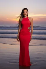 Vestido largo de fiesta color rojo, con cuello halter y diseño ajustado al cuerpo. Presenta una abertura lateral en la cintura con detalle de argollas metálicas.