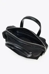 Bolso de mano tipo 'city' o 'bowling' pequeño, confeccionado en nylon negro. Posee asas dobles de material contrastante (posiblemente cuero o efecto charol) y una correa extraíble para llevar al hombro o cruzado.