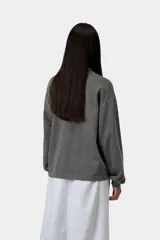 Remera de manga larga gris oscuro de corte holgado, confeccionada en algodón orgánico con efecto desteñido. Presenta cuello redondo y una pequeña etiqueta cuadrada en el dobladillo inferior.