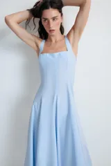 Vestido midi de color celeste con escote cuadrado y tirantes anchos. Presenta un diseño entallado en el torso con falda acampanada terminada en godets que aportan volumen y movimiento. Incluye cierre lateral con cremallera oculta.
