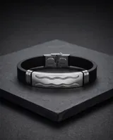 Pulsera de diseño moderno con placa central de acero inoxidable con detalle de ondas grabadas y correa de goma negra.