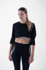 Top negro corto con mangas largas, cuello redondo y detalle de flecos de strass colgantes en el ruedo.