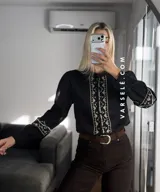 Camisa de manga larga color blanco con bordados geométricos en negro a lo largo de la botonadura frontal y en los puños. Presenta cuello mao y cierre frontal con botones.