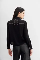 Camisa de estilo texano en color negro, con mangas largas, cuello camisero y cierre frontal con botones metálicos. Presenta un diseño con tachas termo fijadas en la zona del canesú delantero.