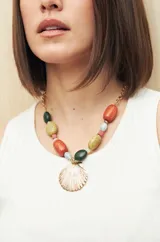 Collar corto con cadena dorada y cuentas de colores en tonos verde, naranja, amarillo y celeste. Dije central con forma de concha marina.