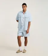 Camisa masculina de jeans celeste con estampa de rayas verticales, corte boxy, cuello inglés, manga corta, cierre abotonado y bolsillos frontales.