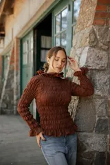 Blusa de muselina de algodón color marrón, con diseño completamente fruncido, cuello alto con volados, mangas largas con puños acampanados y terminación con volado en el ruedo.