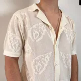 Camisa de tejido de punto calado color negro, con cuello solapa, cierre frontal de botones y mangas cortas.