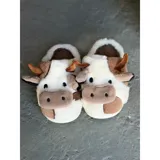 Pantuflas de peluche con diseño de vaca, confeccionadas en piel sintética suave. Cuentan con suela de goma antideslizante y diseño abierto en el talón.