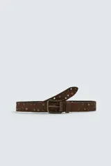 Cinturón de cuero gamuzado color marrón, con aplicación de tachas metálicas circulares y ojales decorativos. Cuenta con hebilla metálica de estilo envejecido y pasador a juego.