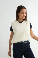 Chaleco de punto color crema con escote en V, sin mangas y diseño decorado con pequeñas perlas aplicadas en toda la superficie.