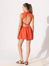 Vestido corto color naranja con textura floral en relieve, cuello alto, corte a la cintura y falda balloon. Presenta aberturas laterales.