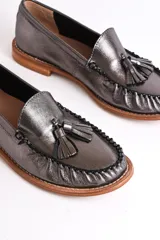 Mocasines negros de cuero con borlas y costuras decorativas.