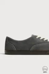 Zapatilla deportiva barefoot fabricada en piel con acabado serraje de color marrón, con cordones en contraste y suela fina de goma.