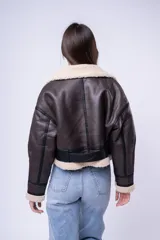 Campera tipo gamulán de cuero sintético marrón oscuro con interior y detalles de corderito sintético en cuello y puños. Presenta cierre frontal, bolsillos laterales con cierre y correas ajustables en el cuello.