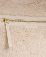 Bolso tote de sherpa color crema, con asas de mano y correa bandolera ajustable. Cuenta con cierre de cremallera y bolsillos internos.