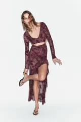 Vestido midi confeccionado en tul semitransparente con diseño de flores flocadas. Presenta escote en pico, mangas largas, aberturas laterales tipo cut out en la cintura y bajo asimétrico con volados. Incluye forro interior y cierre en la espalda con lazadas.