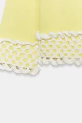Chaqueta de punto color amarillo claro, con cuello redondo y mangas por debajo del codo. Presenta detalles de acabado en tejido crochet blanco en el ruedo y los puños, con cierre frontal de botones forrados al tono.