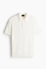 Remera polo de punto mezcla de algodón y viscosa, color blanco, de manga corta con cuello clásico y tapeta de tres botones. Presenta un sutil diseño texturizado en la trama y corte ajustado.