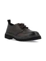 Zapato de cuero marrón oscuro con cordones, suela track robusta y costuras pespunteadas visibles alrededor de la base.