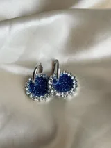 Aros colgantes con forma circular, hechos de resina color lila y borde de strass plateado. El aro es de acero quirúrgico plateado.