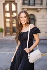 Vestido midi de color negro, con escote cuadrado, mangas cortas abullonadas y detalle de frunces con lazo en el centro del pecho. Presenta una silueta entallada en la cintura y falda con caída fluida.