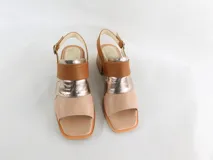 Sandalias de cuero color nude, con tiras cruzadas en dorado y marrón, taco de madera y pulsera al tobillo con hebilla.