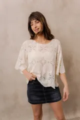 Blusa de punto calado color blanco, con diseño geométrico y floral transparente, escote redondo y mangas tres cuartos amplias de calce relajado.