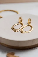Aros colgantes dorados con forma ovalada irregular y acabado martillado. Fabricados en acero quirúrgico hipoalergénico con baño de oro.