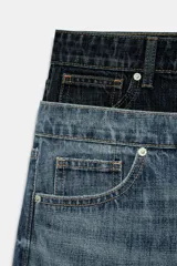 Jeans de tiro bajo confeccionados en denim, con diseño holgado y bajo con vuelta. Presentan el detalle de doble cinturilla en tonos contrastantes de azul, cierre frontal con cremallera y botón metálico, y cinco bolsillos clásicos.