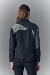 Campera de denim rígido con diseño de recortes en tonos gris y negro. Presenta cuello camisero, cierre frontal con botones metálicos, bolsillos con solapa en el pecho y corte recto.