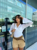 Remera blanca de encaje con diseño cruzado tipo wrap, mangas largas con terminación acampanada y detalle de bordado floral a tono. Presenta un ajuste al cuerpo con lazo lateral y borde con terminación delicada en el escote.