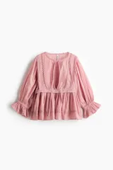 Blusa rosada de algodón con ribetes de encaje, cuello redondo con abertura en V y tiras para anudar, mangas largas abullonadas con puños elásticos y terminación peplum con vuelo.