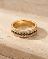 Anillo de bronce con baño de oro, diseño de banda ancha con una hilera central de circonias azules y hileras laterales de circonias transparentes.