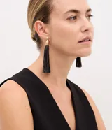 Par de aros colgantes con base metálica dorada y flecos largos de tiras finas de poliuretano color negro.