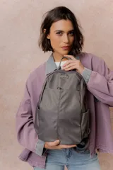 Mochila gris de diseño minimalista, con compartimento principal con cierre, bolsillo frontal con cierre oculto, bolsillos laterales y tiras regulables. Cuenta con el logo de la marca en la parte superior frontal.