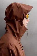 Cazadora deportiva color marrón confeccionada en tejido técnico de tres capas con membrana impermeable. Cuenta con cuello alto con capucha ajustable, mangas largas con puños reforzados ajustables, aberturas con cremallera en axilas, bolsillos frontales con cremallera y bajo ajustable con elásticos laterales.