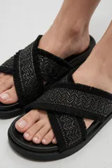 Sandalias planas color crudo con tiras cruzadas de tejido textil con diseño geométrico y detalles de flecos en los bordes.