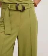 Pantalón pantalona color verde oliva, confeccionado en tejido orly con viscosa certificada. Presenta trabillas largas en la cintura, cierre tradicional, bolsillos y frisos delanteros. Incluye cinturón largo de tejido con hebilla irregular.