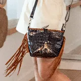 Bandolera negra con textura tipo piel de cocodrilo, flecos marrones en los laterales y herrajes dorados.