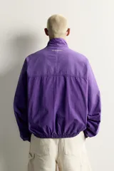 Cazadora relaxed fit de denim de algodón en color violeta, con efecto lavado, cuello alto, cierre frontal de cremallera y bolsillos en las costuras laterales. Presenta puños y dobladillo elásticos.