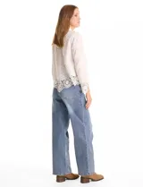 Camisa de algodón con bordado suizo, cuello con solapa y cierre frontal con botones. Presenta mangas largas con terminación de encaje calado y un ruedo asimétrico en pico con un amplio galón de encaje.