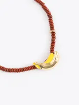 Collar de cuentas de piedra marrón con dije en forma de banano dorado y amarillo. Cuenta con cadena de extensión dorada.
