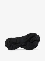 Zapatilla urbana de diseño vanguardista en color negro, con estructura de malla y superposiciones de paneles de goma texturizados. Presenta cierre con tiras autoadherentes y suela robusta con diseño ergonómico.