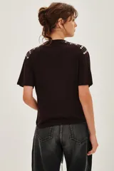 Remera de viscosa color negro, con cuello redondo y mangas cortas. Presenta un detalle decorativo de apliques metálicos en forma de corazón dispuestos en líneas sobre los hombros.