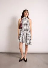 Vestido corto blanco con lunares negros, cuello halter y corte evasé.