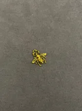 Dije pequeño con forma de abeja en color dorado, con detalles grabados en las alas y el cuerpo.