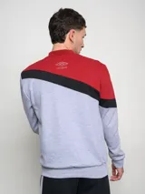 Buzo de hombre con diseño de bloques de color, combinando rojo en la parte superior de los hombros y gris melange en el cuerpo. Presenta una franja diagonal negra con el logo Umbro en blanco cruzando el pecho.